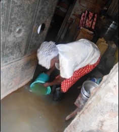 Janet bends down to scoop some of the dirty water that is mixed with sewage and waste from the nearby rubbish damp